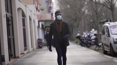 Black man wearing covid face mask walking outside in city downtown