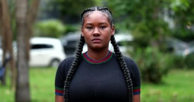 African young woman standing outside looking at camera. Real people series, casual black girl