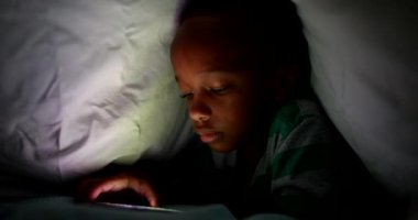 Genç bir çocuk gece battaniyenin altında cep telefonu ekranına bakıyor.