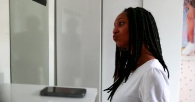 African American teen girl picking up cellphone call while looking at herself in mirror. Person answers cellphone