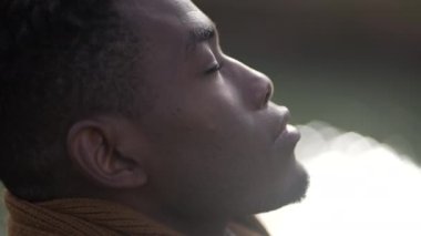 Black man taking a deep breath outside and opening eyes looking up at sky smiling feeling free