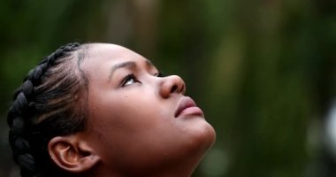 Hopeful African woman standing outside looking at sky in contemplation