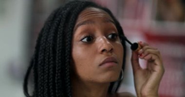 Mixed race adolescent girl applying make-up, looking at mirror