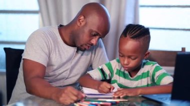 Black father helping son with homework at home. Mixed race parent tutoring child