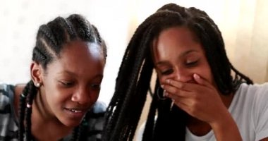 Girlfriend sharing cellphone screen. Black sisters laughing together, girls covering hands with mouth in shock