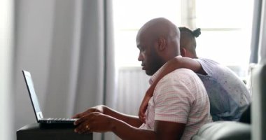 Black father working from home in front of laptop, little boy wanting dad attention