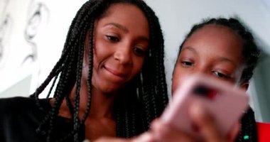 Adolescent black girls looking at smartphone device smiling