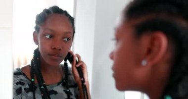 Afrikalı kız aynanın önünde kendini kontrol ediyor. Ergen kız ayakta saçlarıyla oynuyor.