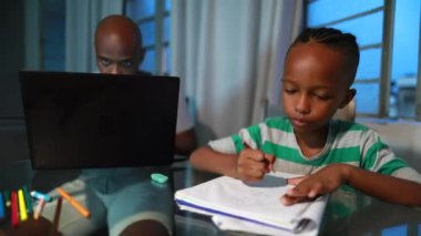 African american father working from home using laptop computer, black child son doing homework