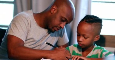 Evde ödev yapan küçük bir çocuk, Afrikalı bir baba oğlana çalışmasında yardım ediyor.
