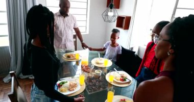 African black family giving thanks praying before meal and sitting down to eat lunch