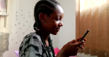Afrikalı genç kız akıllı telefon cihazında mesaj yazıyor. Siyah genç cep telefonu kullanıyor.