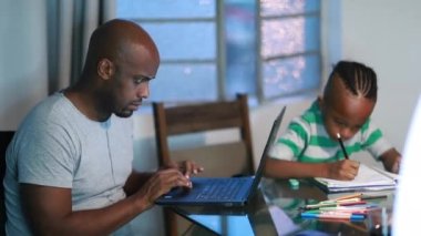 Father in front of laptop computer, son child drawing on notebook, Black mixed race african family
