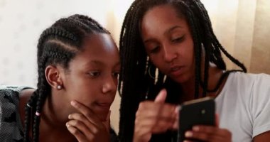 Teen friend showing cellphone screen to sister. Black African ethnicity