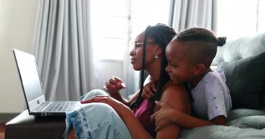 Anne laptopun önünde oğluyla çalışmaya çalışıyor. İlgi istiyor, ebeveyn evde çalışıyor.