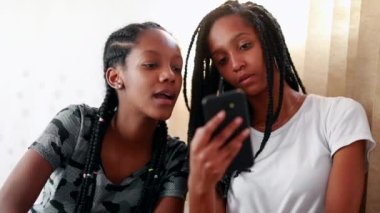 Girls gossiping on social media covering face with mouth. Black African sisters sharing screen