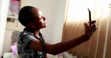 Teenager girl taking selfie in adolescent room. Mixed race black ethnicity