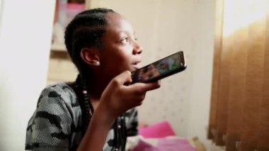 Black African teen girl using cellphone in adolescent room