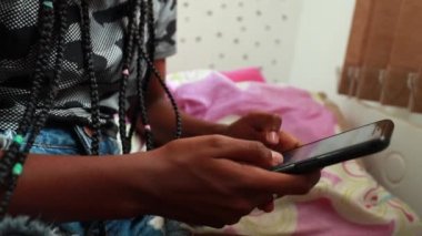 Black African teen girl using cellphone in adolescent room