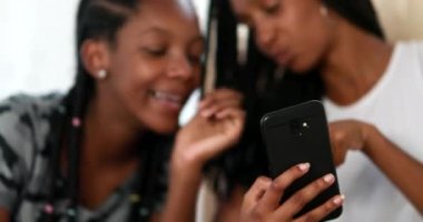 Two black girls looking at cellphone screen laughing together. African American ethnicity