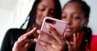 Akıllı telefon cihazı tutan siyah genç kızlar. Cep telefonu ekranına bakan Afrikalı kardeşler