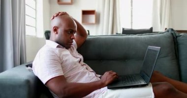 Merkezi ofisteki kanepeye yaslanmış dizüstü bilgisayarla serbest çalışan ciddi Afrikalı bir etnik adam.