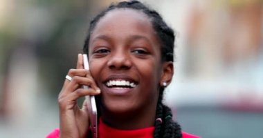 Happy black teen girl smiling and laughing talking on phone outside