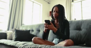upset black teen girl at home sofa looking at cellphone device feeling frustration