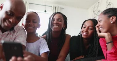 Baba çocuklara cep telefonu ekranını gösteriyor, aile bir araya gelip akıllı telefona bakıyor.