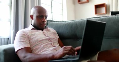 Evinde dizüstü bilgisayar kullanan Afrikalı bir adam.