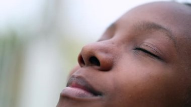 African girl closing and opening eyes in meditation. Black teen face looking up to sky in contemplation