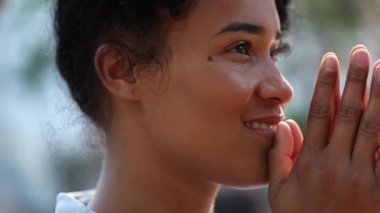 Thoughtful pensive black woman praying smiling outside