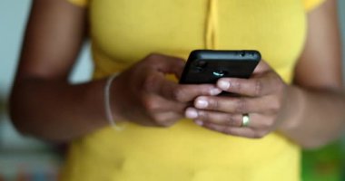 Genç siyahi kadın elinde akıllı telefon cihazıyla mesaj atıyor ve gülümsüyor.