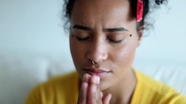 Spiritual mixed race woman putting hands on chest praying at home and smiling