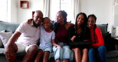 Kanepede oturan Afrikalı aile kameraya, ebeveynlere ve çocuklara gülümsüyor.