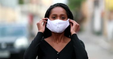 African girl putting covid-19 face mask prevention outside in street staring camera