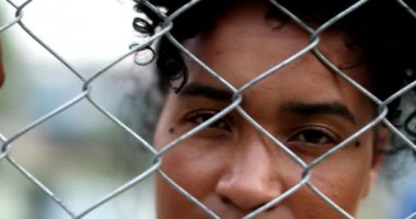 Sad black woman seen through metallic fence cage