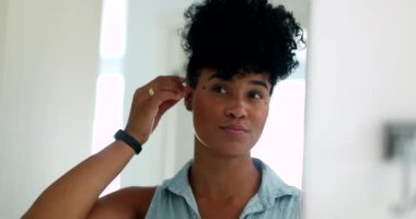 Young black woman looking at herself in mirror adjusting hair