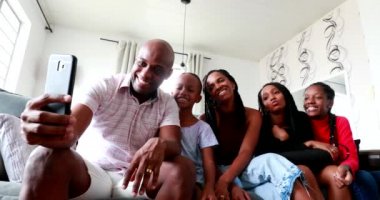 Black family taking selfie with cellphone at home sofa. Black father holding smartphone with children and wife