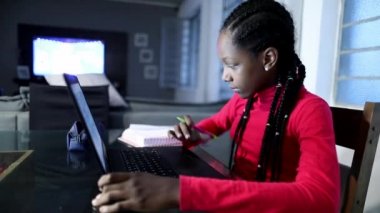 Black teen girl studying at home in front of computer laptop