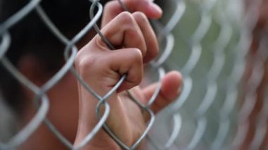 Person holding hands into metal fence outside, close-up black woman hand leaning on metallic wall gate