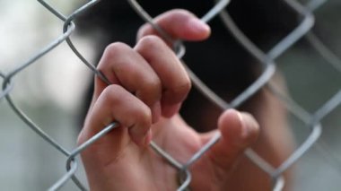 Hand holding into metal fence. Close-up black hands leaning on security gate