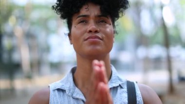 Hopeful Black african woman praying outside, feeling happy and faithful