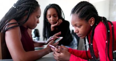 African family looking at cellphones screens. Black mother and teenager daughters staring at devices