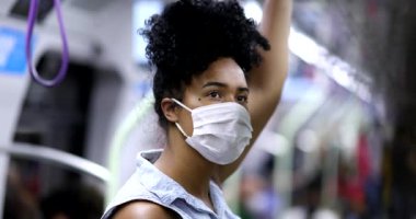 Metroda giderken elinde tırabzan, yüzünde maske olan genç siyahi bir kadın.