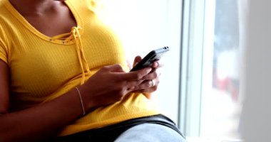 Siyah Afrikalı kadın akıllı telefon cihazıyla evde yazı yazıyor.