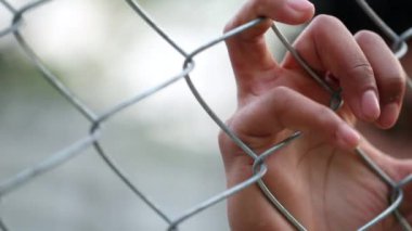 Hand holding into metal fence. Close-up black hands leaning on security gate