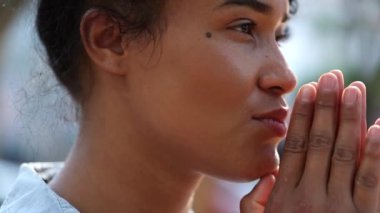 Black woman praying outside feeling hopeful. Mixed ethnicity girl being thankful and grateful