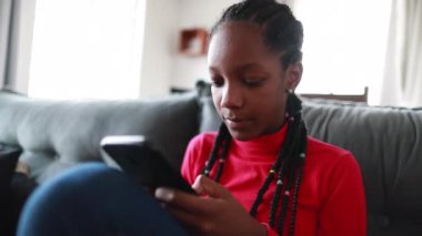 Teen black girl using cellphone at home sofa
