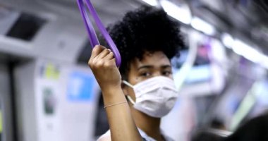 Afrika kökenli Amerikalı kadın salgın sırasında metro tırabzanı tutuyor.